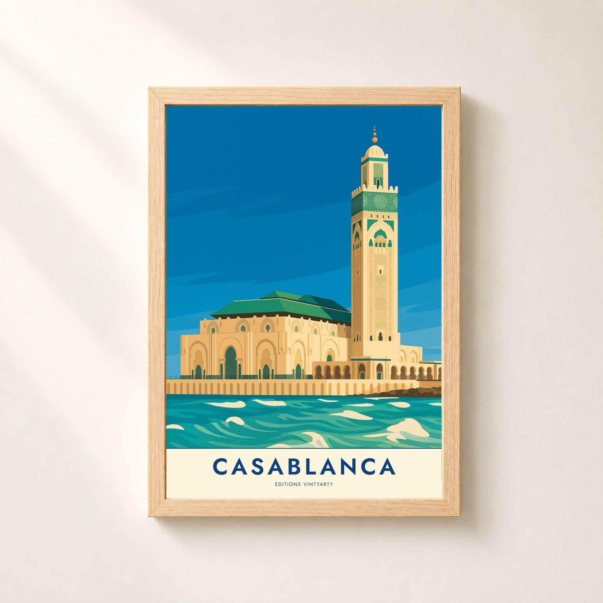 Affiche Casablanca dans un cadre en chêne naturel sur un mur blanc, mosquée Hassan II et son minaret face à l'océan Atlantique.