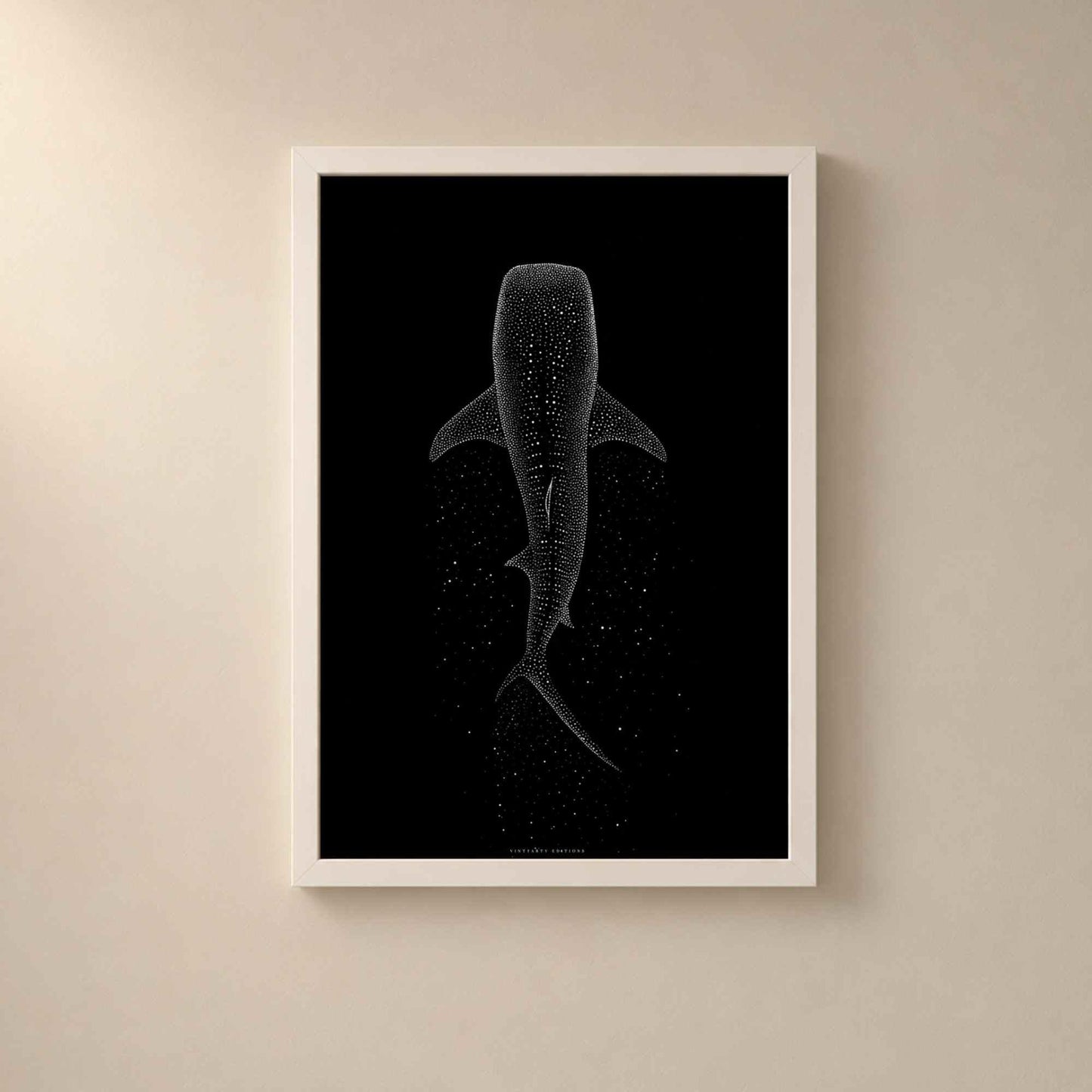 Affiche requin baleine dans un cadre en bois blanc sur un mur beige, silhouette de l'animal en pointillisme blanc vue de dessus sur fond noir.