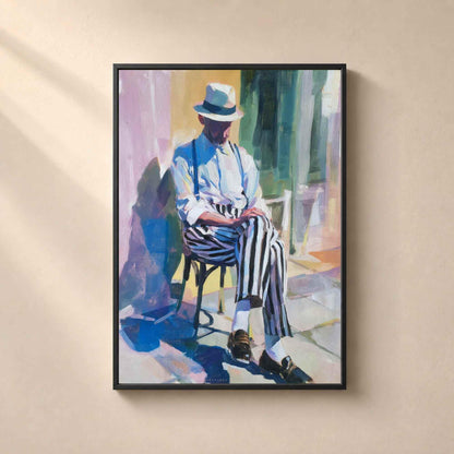 Affiche dans un cadre en métal noir fin sur un mur beige, homme assis au chapeau panama et pantalon rayé dans une rue méditerranéenne ensoleillée.