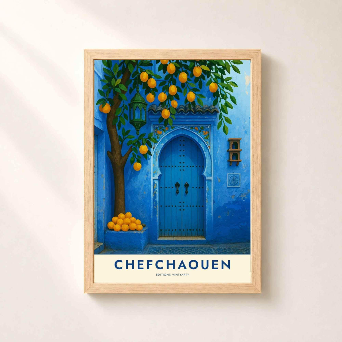 Affiche Chefchaouen dans un cadre en chêne naturel sur un mur blanc, porte marocaine bleue sous un oranger et lanterne verte.