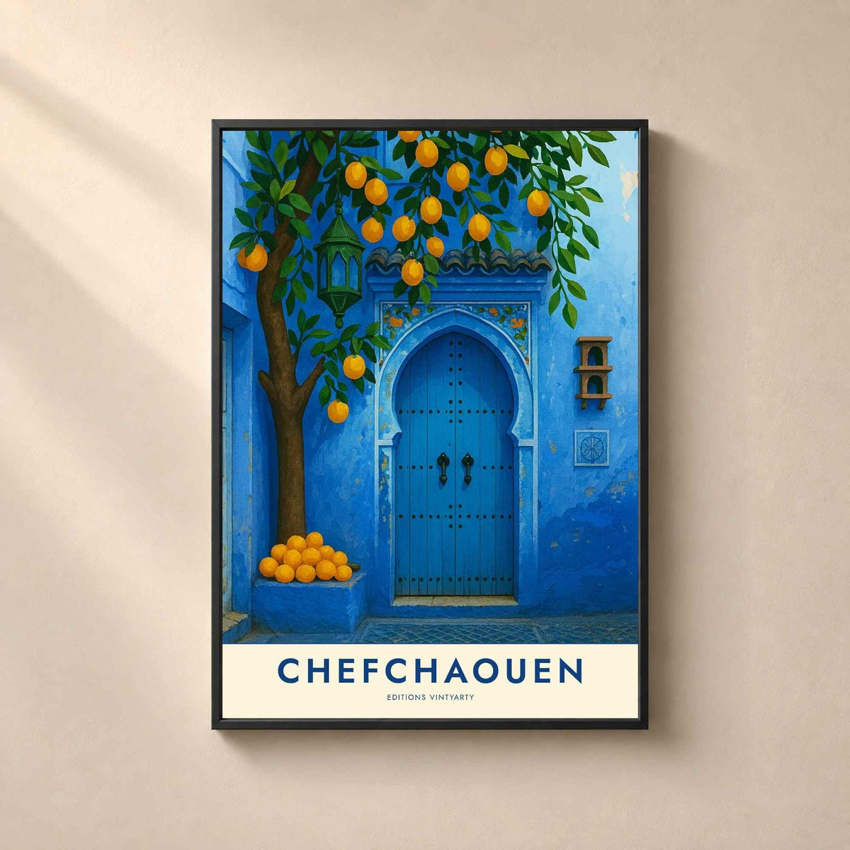 Affiche Chefchaouen encadrée en métal noir fin sur un mur beige, mur bleu de la médina et oranges empilées sur un banc de pierre.