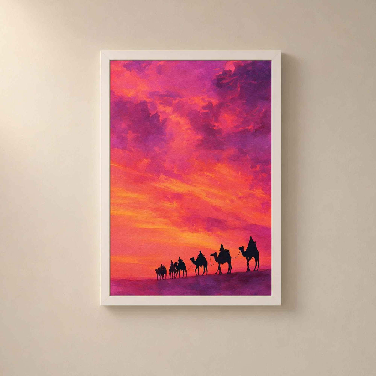 Affiche caravane dans un cadre en bois blanc sur un mur clair, file de dromadaires en silhouette sur une dune sous un ciel de coucher de soleil fuchsia et orange.