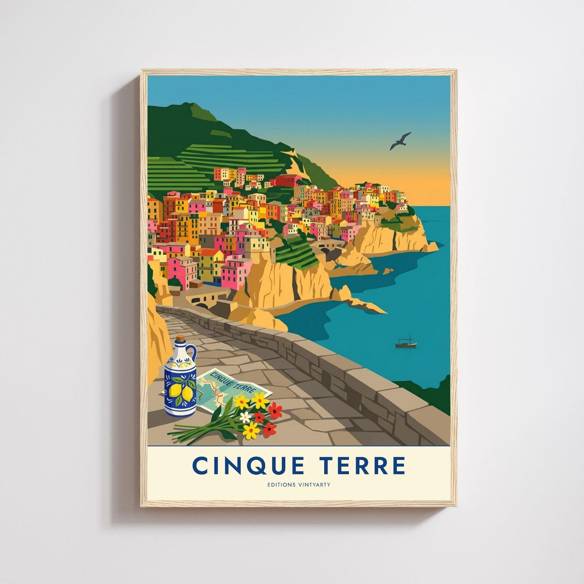 Affiche illustrée de Manarola dans les Cinque Terre, village de maisons roses, jaunes et orange empilées sur une falaise ocre, vignes en terrasses au-dessus, mer turquoise avec une barque au mouillage, chemin dallé et muret de pierre au premier plan avec une bouteille en céramique bleue à motif de citrons, une carte dépliée et un bouquet de fleurs.