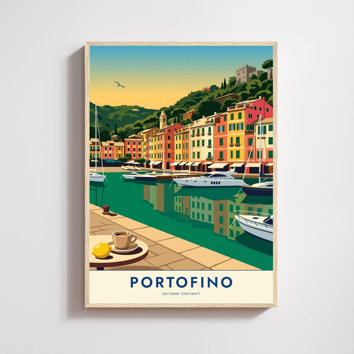 Affiche illustrée du port de Portofino en Ligurie, table ronde de café au premier plan avec une tasse et un citron, quai dallé, eau vert émeraude reflétant les façades rouge, ocre, jaune et rose du port, yachts et voiliers amarrés, colline de pins et cyprès surmontée de la tour du château, ciel dégradé du bleu au doré.
